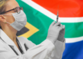 Getty Images | A doctor holding syringe for vaccination against COVID-19, in front of a South African flag.