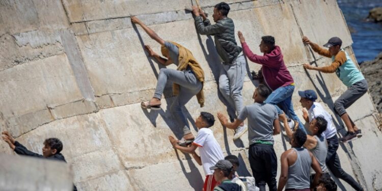 Would-be migants clamber up a sea wall in the Moroccan border town of Fnideq as they seek their chance to slip into the neighboring Spanish enclave of Ceuta | AFP