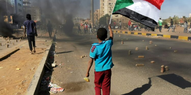 A young boy waves a Sudanese national flag as protesters block a street in the capital Khartoum, during a demonstration against the killing of dozens in a crackdown since last year's military coup, on January 20, 2022 | AFP