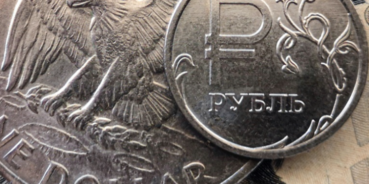 A Russian ruble coin is pictured with US dollar bills and a one dollar coin in Moscow, on March 15, 2022